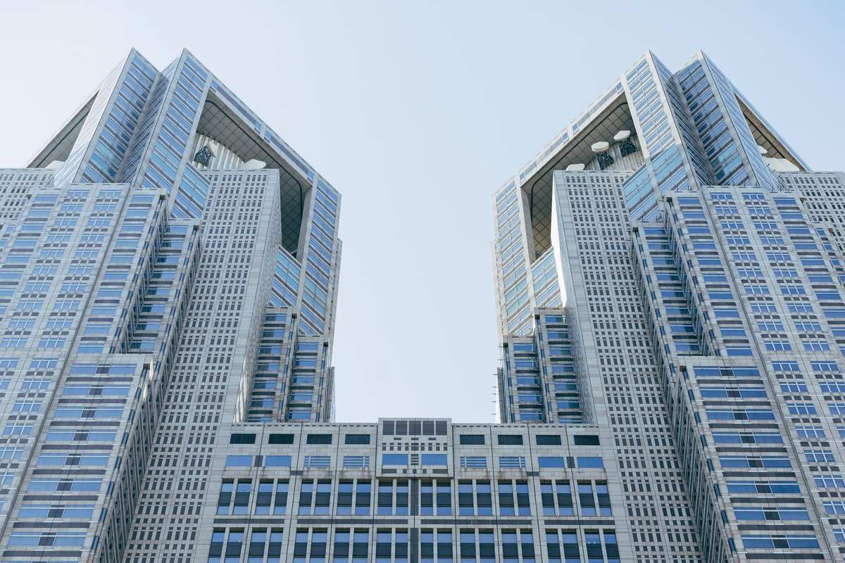 Twin towers of the Tokyo Metropolitan Government Building seen from below against a pale sky