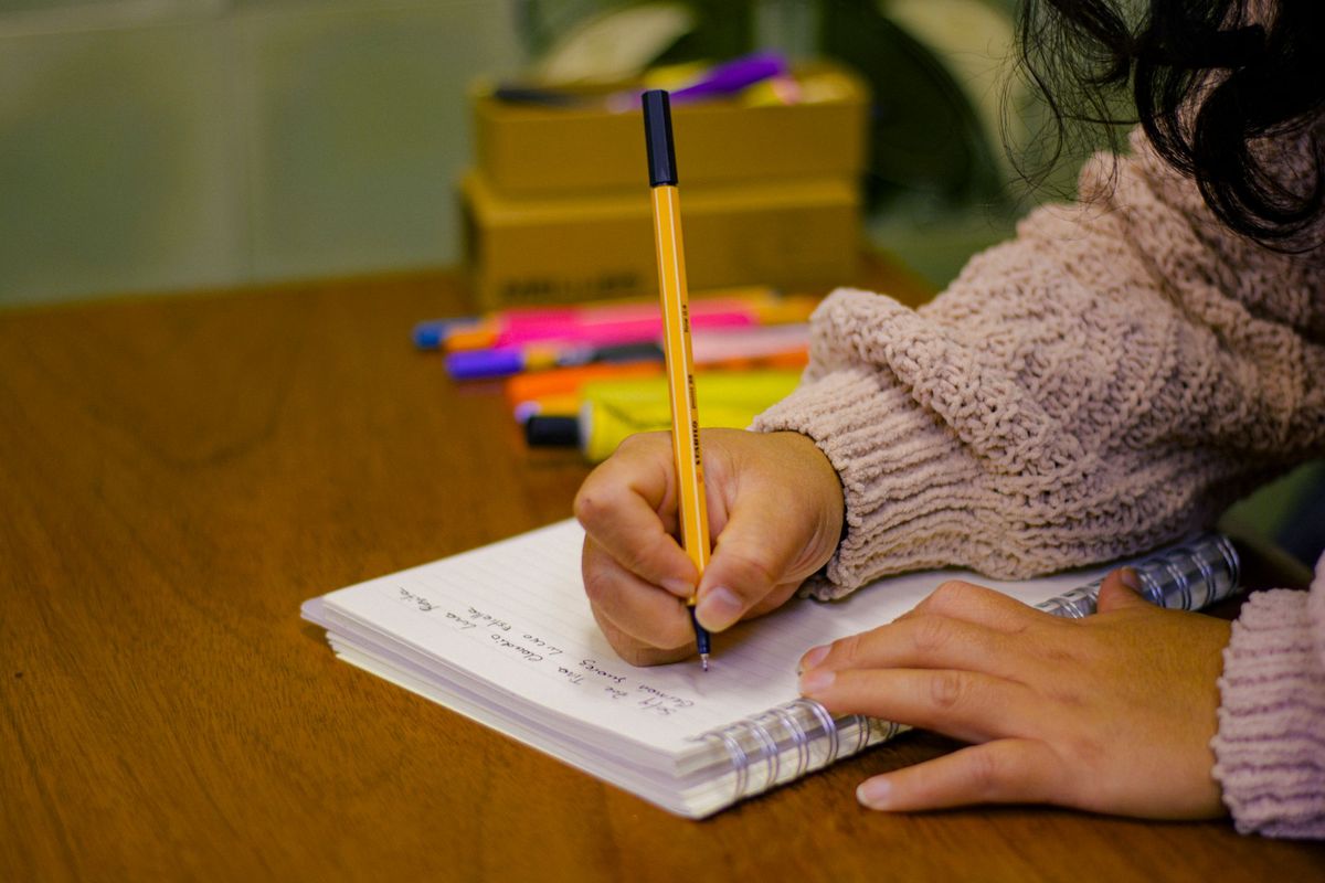 Person writing in a notebook at a wooden desk with colourful highlighters