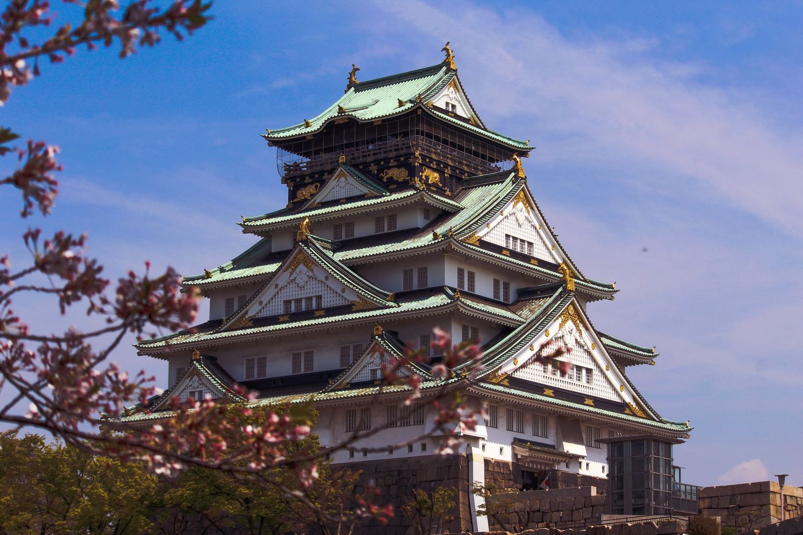 Osaka Castle main keep framed by cherry blossom branches under a blue sky