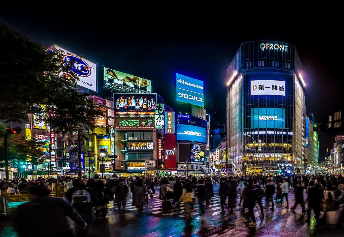 Pedestrians crossing Shibuya Crossing at night beneath illuminated signage in Tokyo